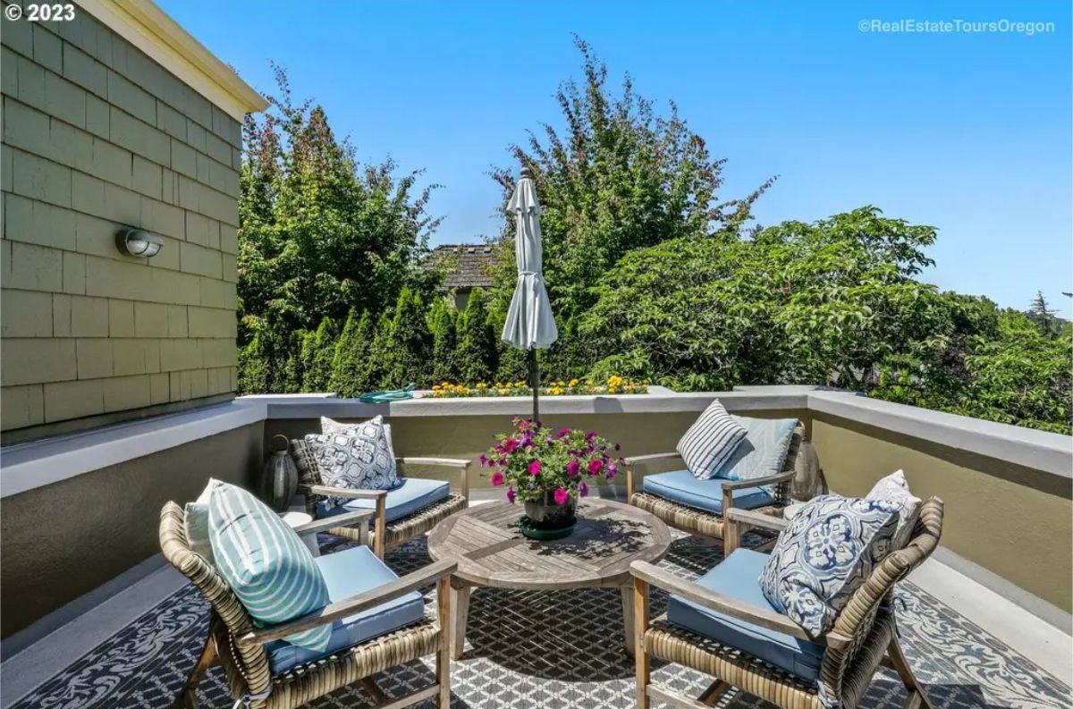 Rooftop terrace features a circular wooden table surrounded by wicker chairs with plush blue cushions.