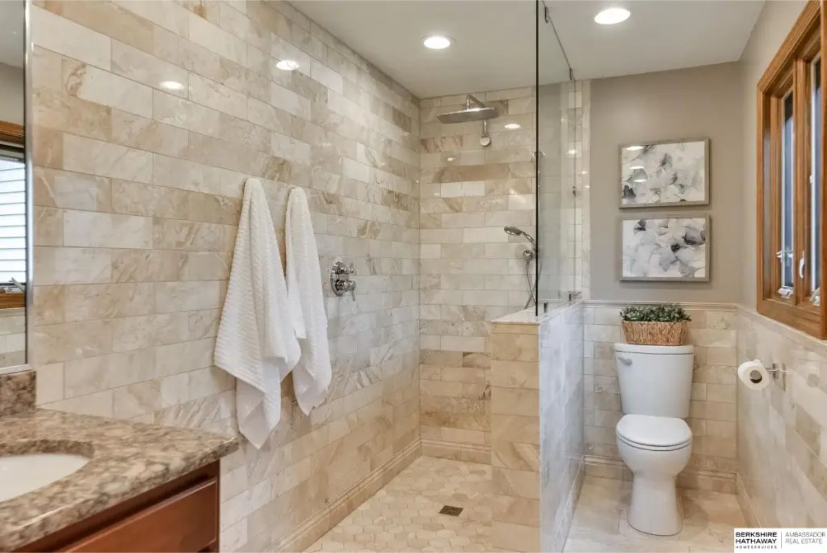 Walk-in shower with marble-patterned tiles and a frameless glass enclosure.