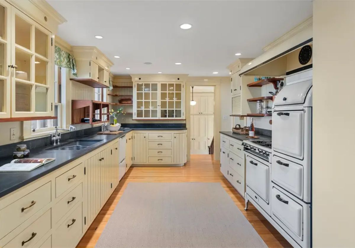 Classic kitchen combines vintage aesthetics with functional design, featuring creamy cabinetry with beadboard detailing and black countertops for a warm, inviting look.