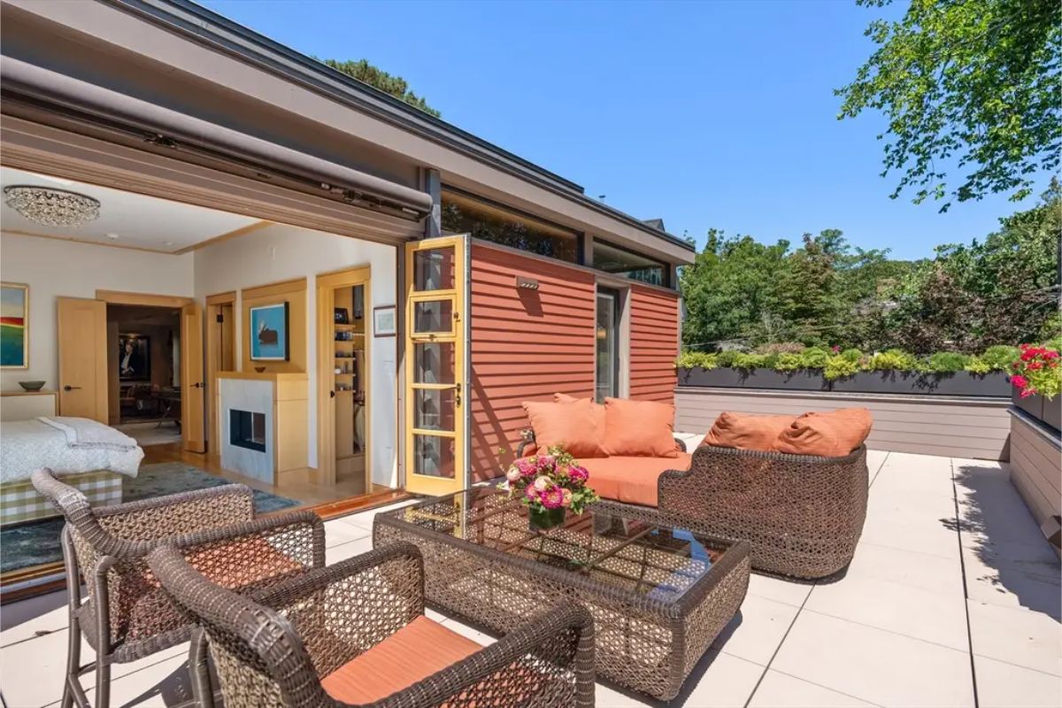 This rooftop terrace offers a perfect retreat with comfortable wicker seating, warm-toned cushions, and lush greenery along the borders.