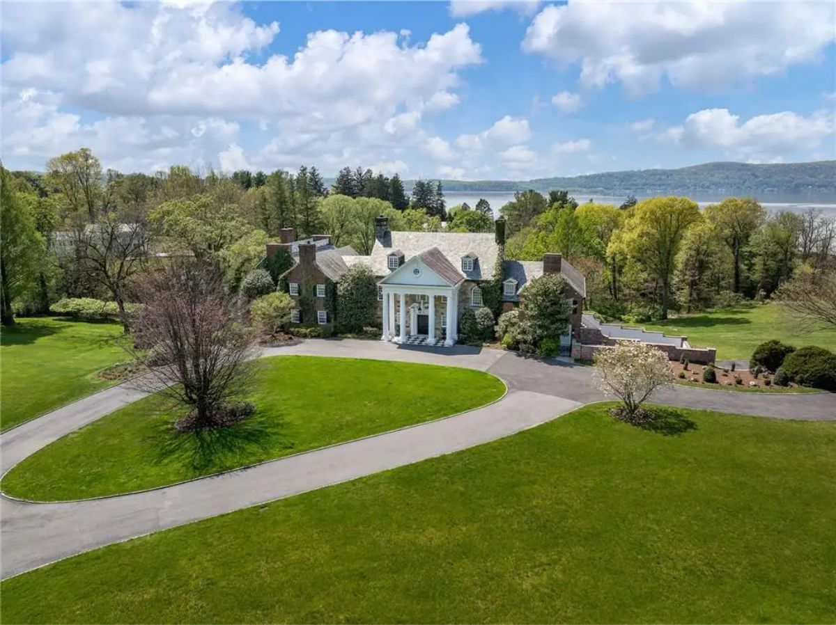 Grand estate with a circular driveway, Georgian architecture, and views of a wooded landscape.
