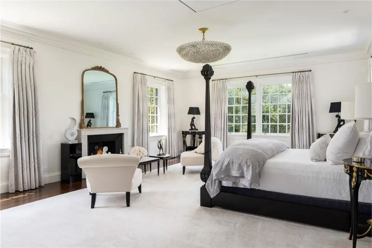 Large bedroom with a four-poster bed, neutral tones, and a decorative chandelier. 