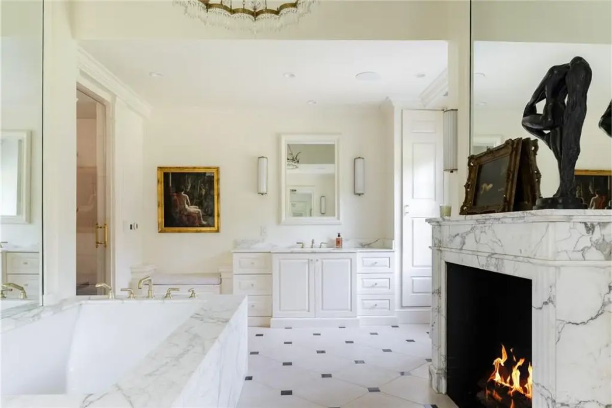 Luxurious bathroom includes marble finishes, a fireplace, a large soaking tub, and dual vanities. 