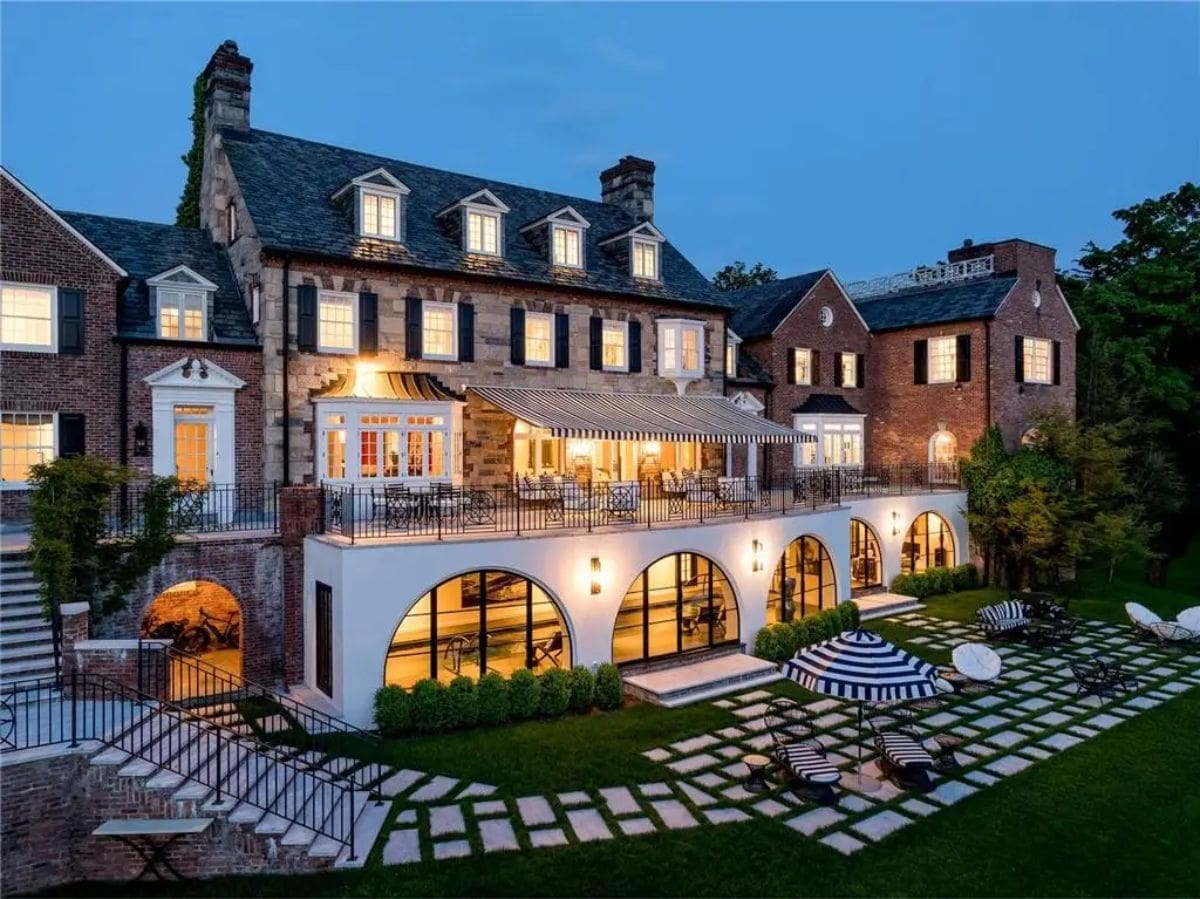Exterior nighttime view emphasizes the grandeur of the property with its lit facade and landscaped grounds. 
