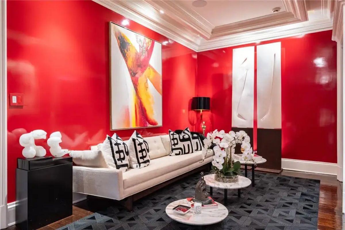Small sitting room with bright red walls, modern artwork, and white upholstered furniture. 