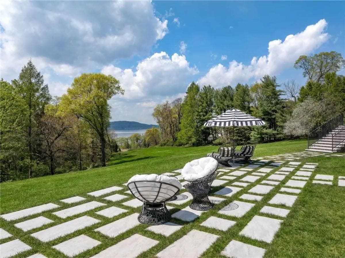 Stone-paved patio overlooks lush lawns and features black-and-white striped seating with umbrellas. 