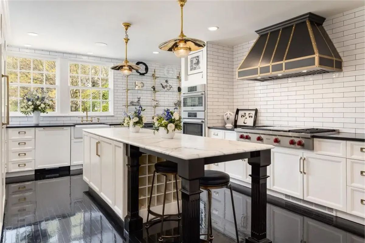 Modern kitchen featuring a white island, gold fixtures, and black-and-white tiled backsplash. 