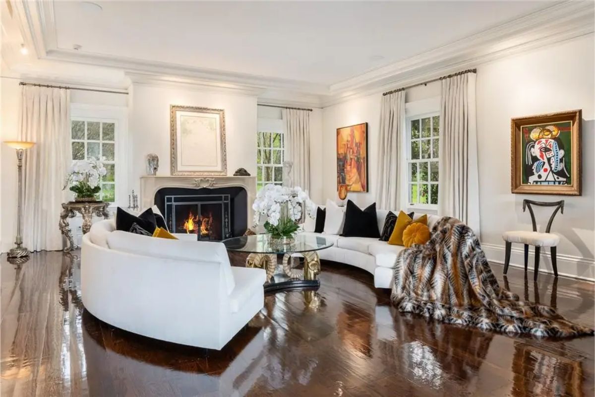 Elegant living room with a curved white sofa, gold-accented decor, and a fireplace. 