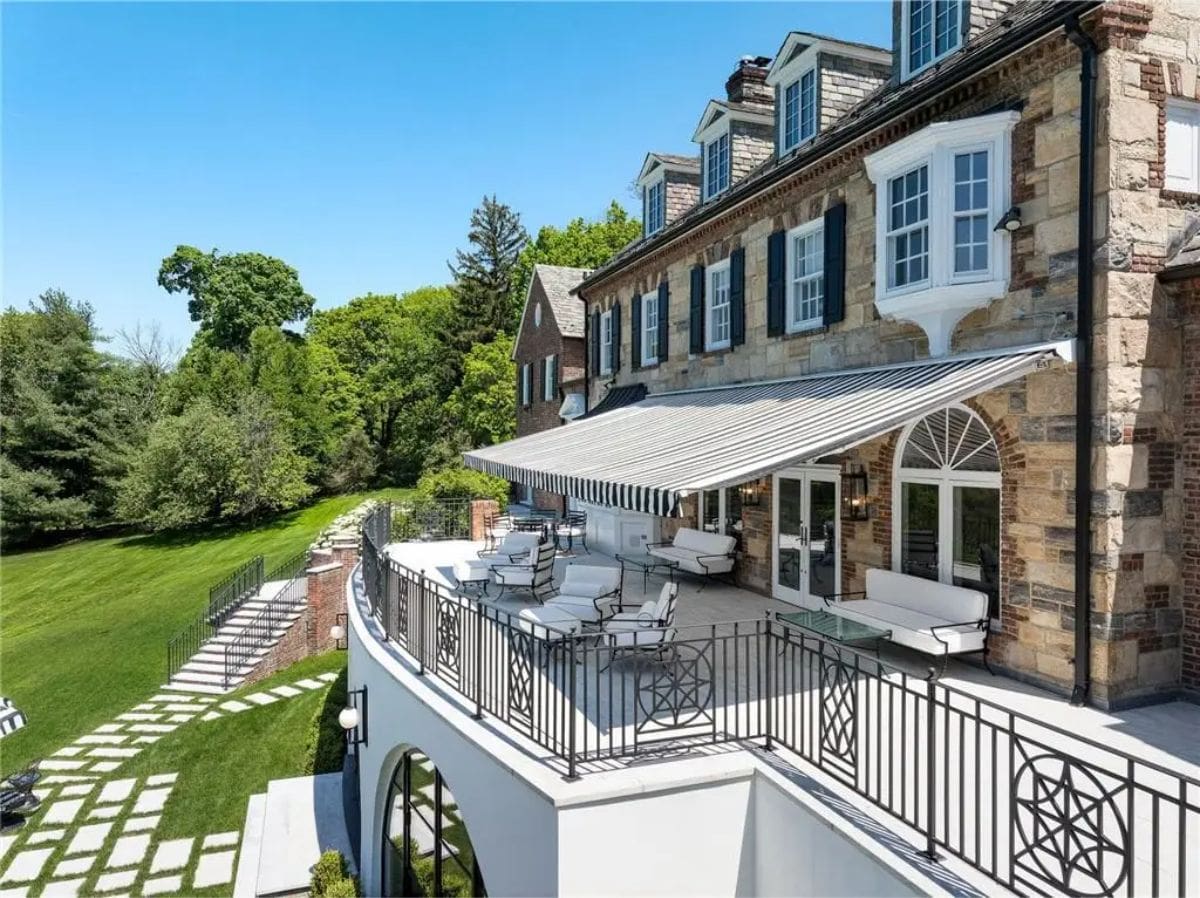 Outdoor terrace includes striped retractable awnings, wrought-iron railings, and white lounge furniture. 