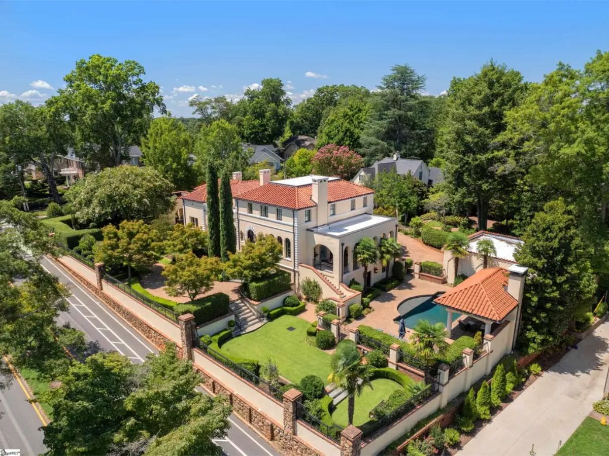Mediterranean home surrounded by manicured gardens and wrought iron fencing.