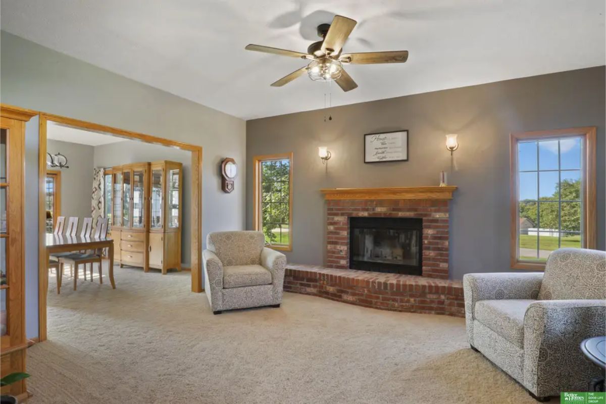 A bright living room features a central brick fireplace framed by a wooden mantle, perfect for creating a warm ambiance