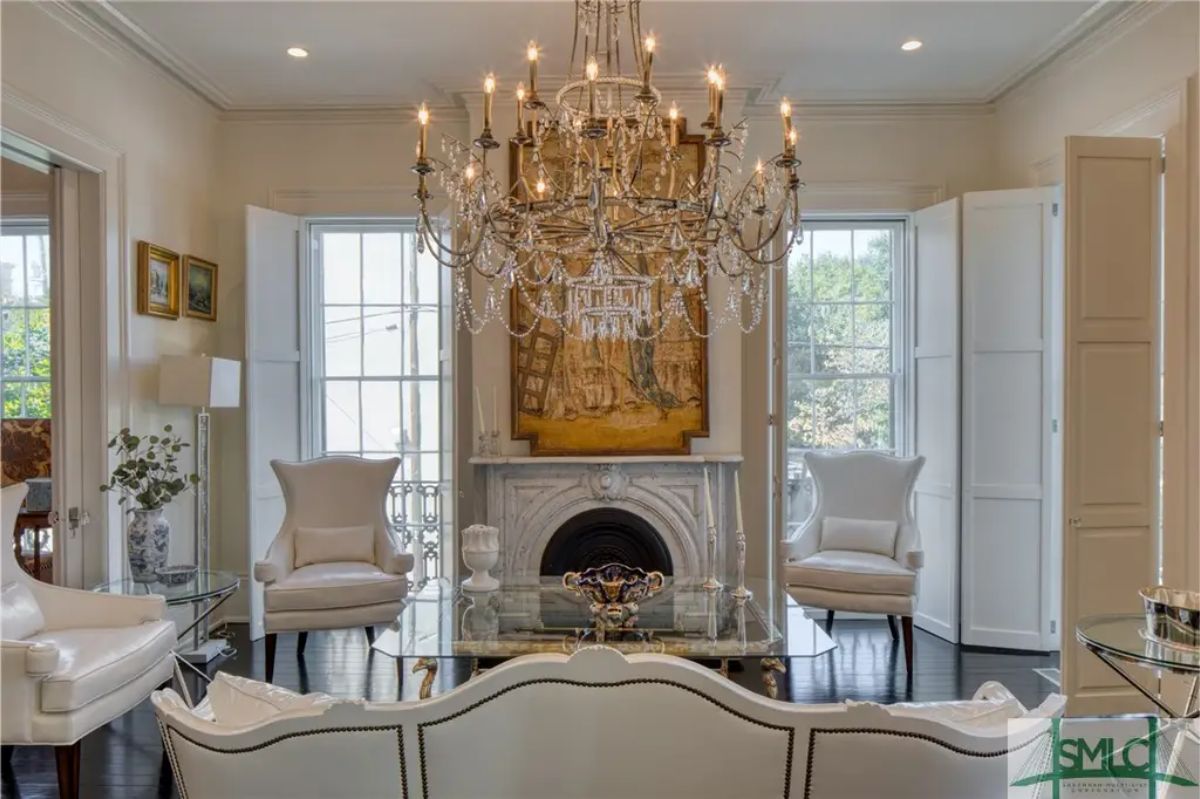 A grand crystal chandelier as the centerpiece, suspended above a glass coffee table and white upholstered seating.
