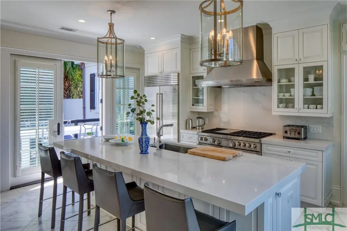 Kitchen features a large white island with an integrated sink, seating for three, and contemporary pendant lighting overhead.