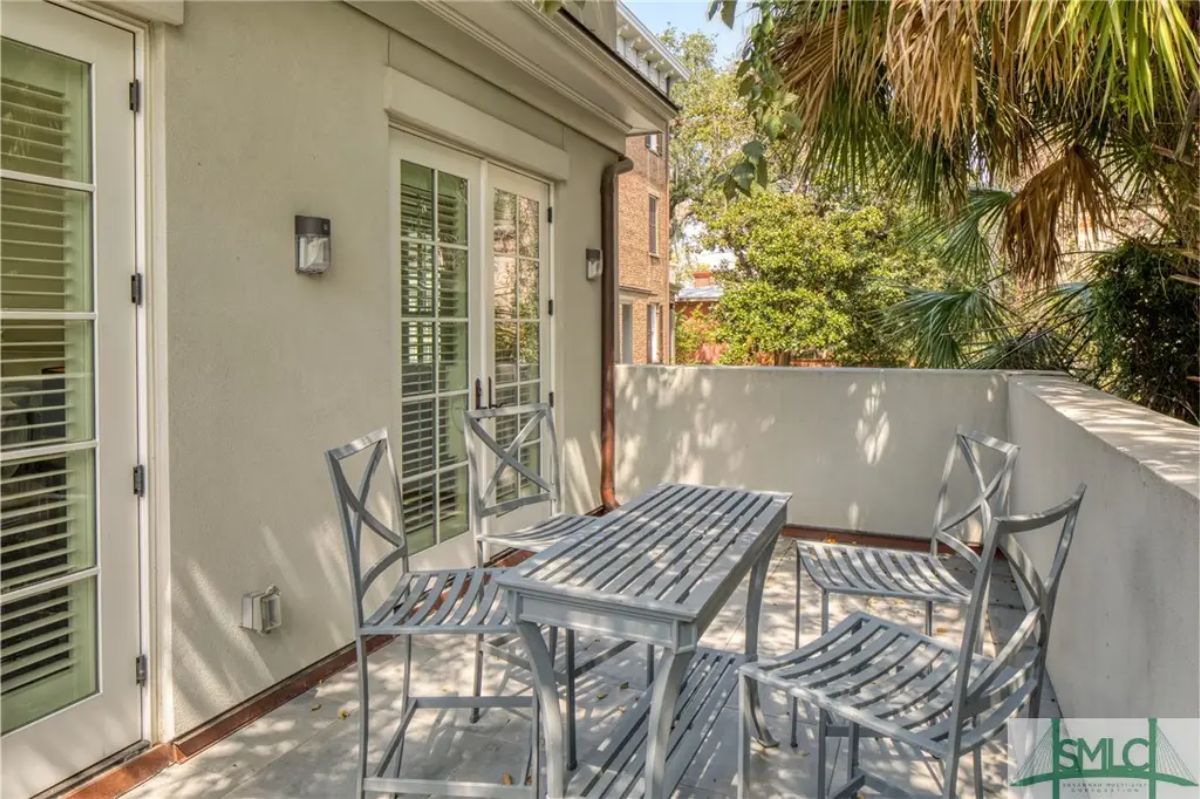 Outdoor patio features a sleek metal dining set with a slatted table and four matching chairs.