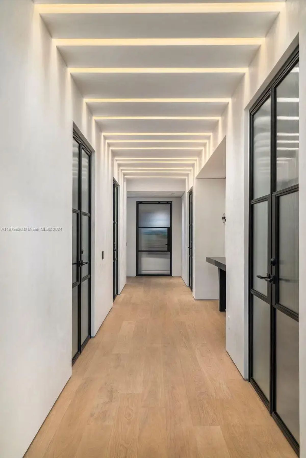 Modern hallway with wooden flooring, glass-paneled doors, and a ceiling featuring geometric recessed lighting. 