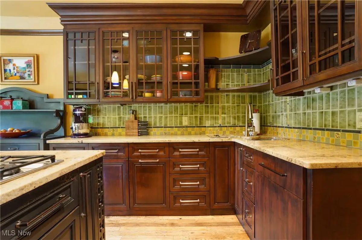 A warm kitchen design features rich wooden cabinets with glass-paneled upper doors for a classic look.