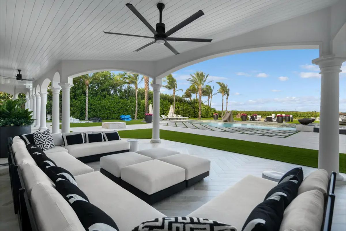 Expansive outdoor lounge with a covered seating area, large plush sofas, and a poolside view with palm trees and ocean breezes. 