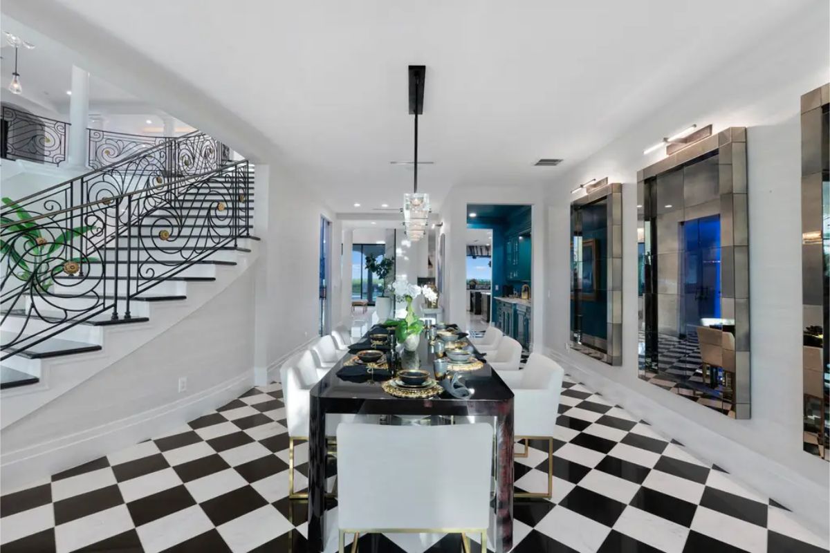 Black and white checkered floor, a long black dining table with white chairs, mirrored panels on the wall, and a staircase to the left.