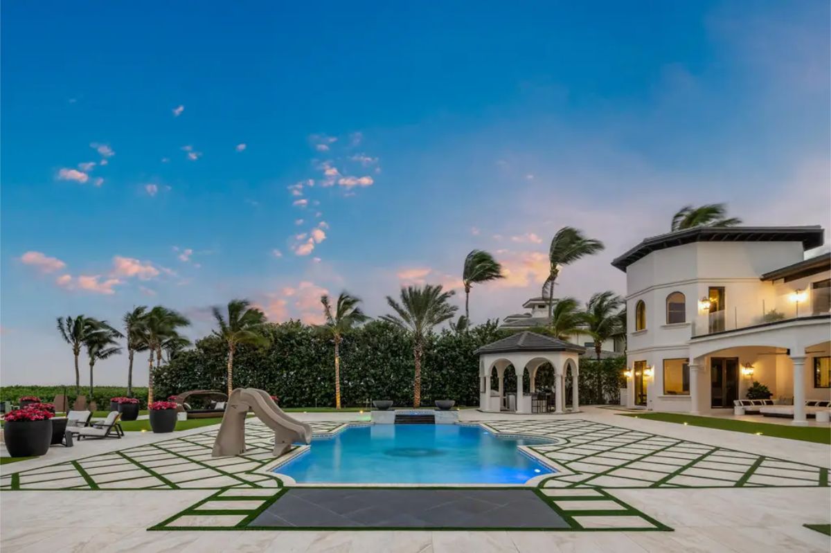 Stunning poolside view at sunset with a cozy gazebo, water slide, and well-manicured greenery. 