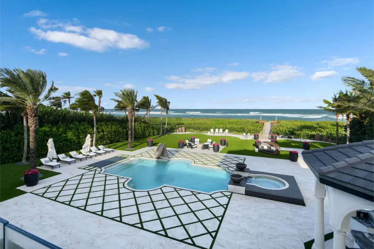 Oceanfront backyard with a sparkling pool, manicured lawns, and a private pathway leading to the beach. 