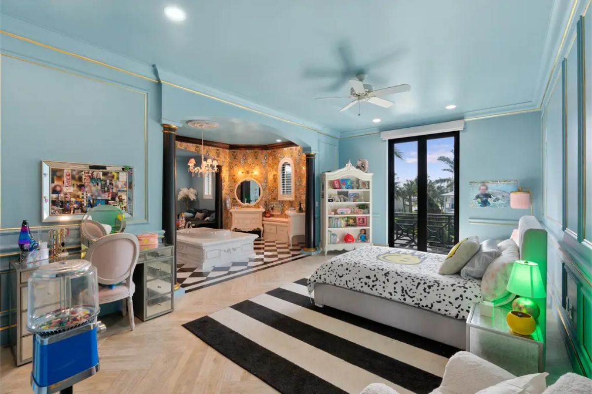 Luxurious bedroom with pastel blue walls, gold accents, and an integrated vanity, opening to a balcony with scenic views. 