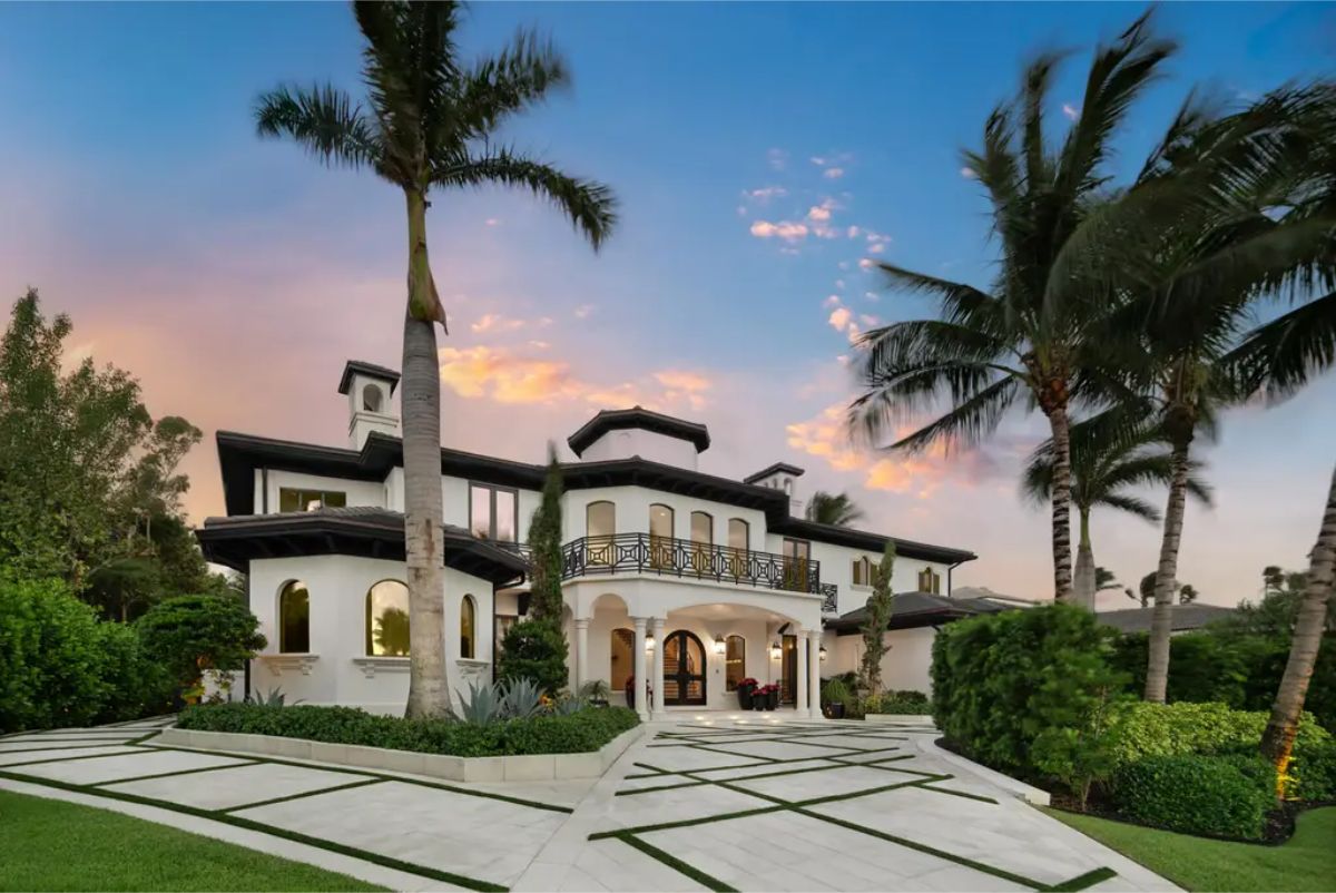 Elegant mansion with a Mediterranean-style façade, arched windows, a manicured driveway, and tall palm trees. 