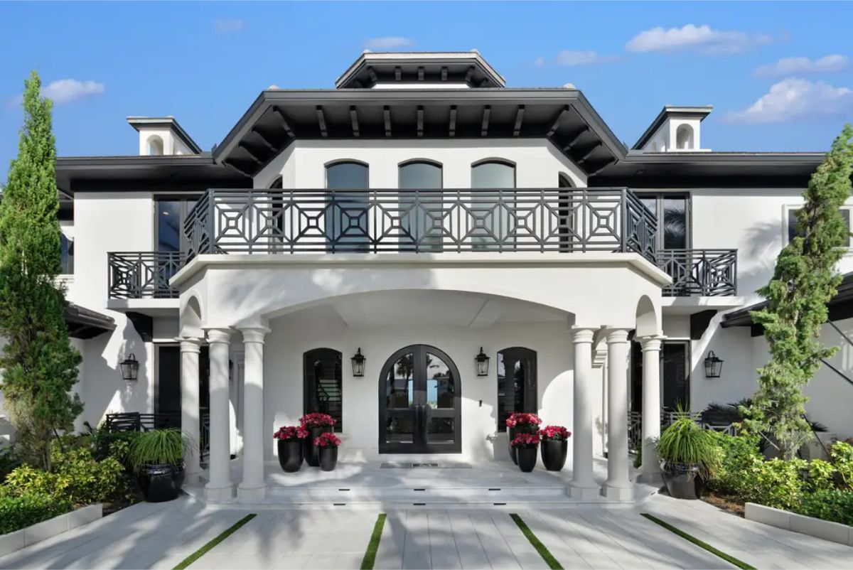 White-columned entrance with black wrought iron balcony railings and symmetrical landscaping. 