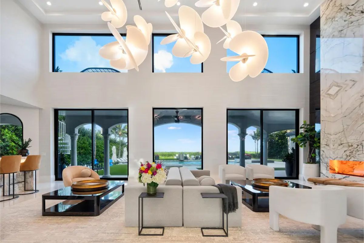 High-ceiling living room with large windows, modern furniture, and sculptural pendant lighting. 