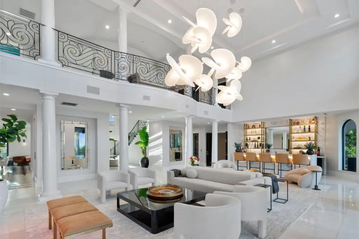 This is a bright, contemporary living room with white walls, tall ceilings, a large decorative light fixture, and a balcony overlooking the space. 