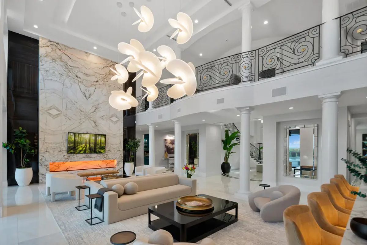 Modern living room with high ceilings, a prominent decorative light fixture, a large marble accent wall, and a staircase leading to an upper level.