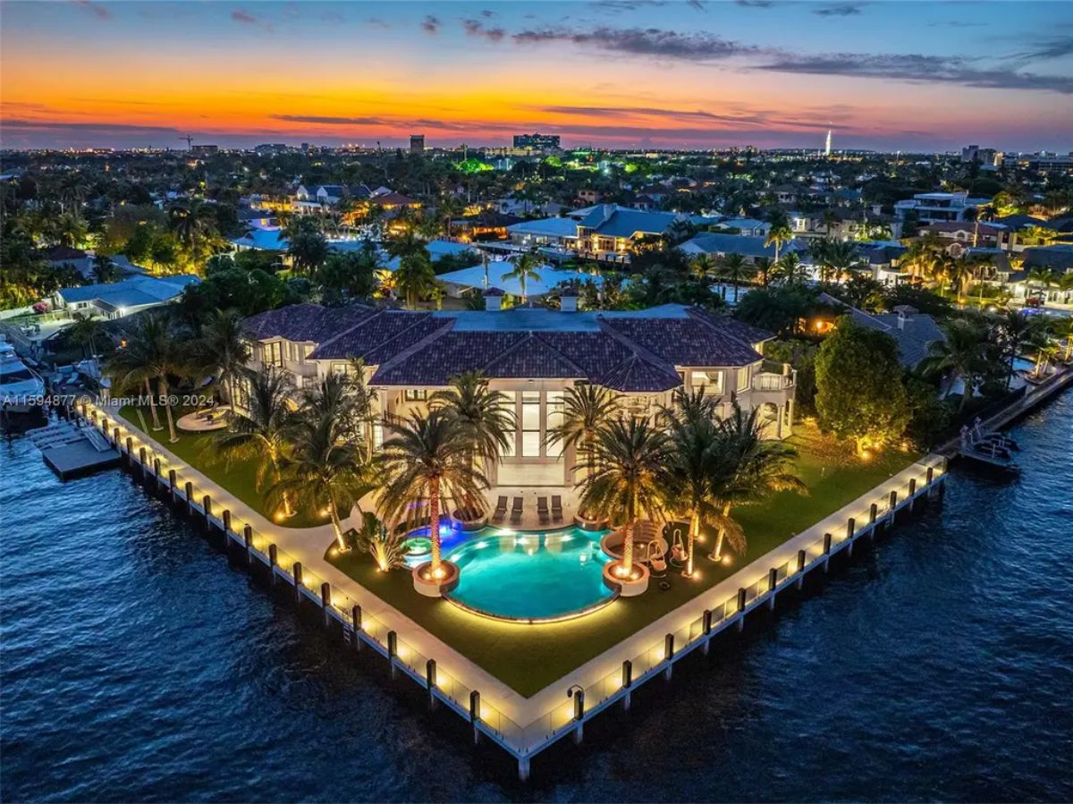 Luxurious waterfront estate with palm trees, a swimming pool, and an illuminated dock at sunset.