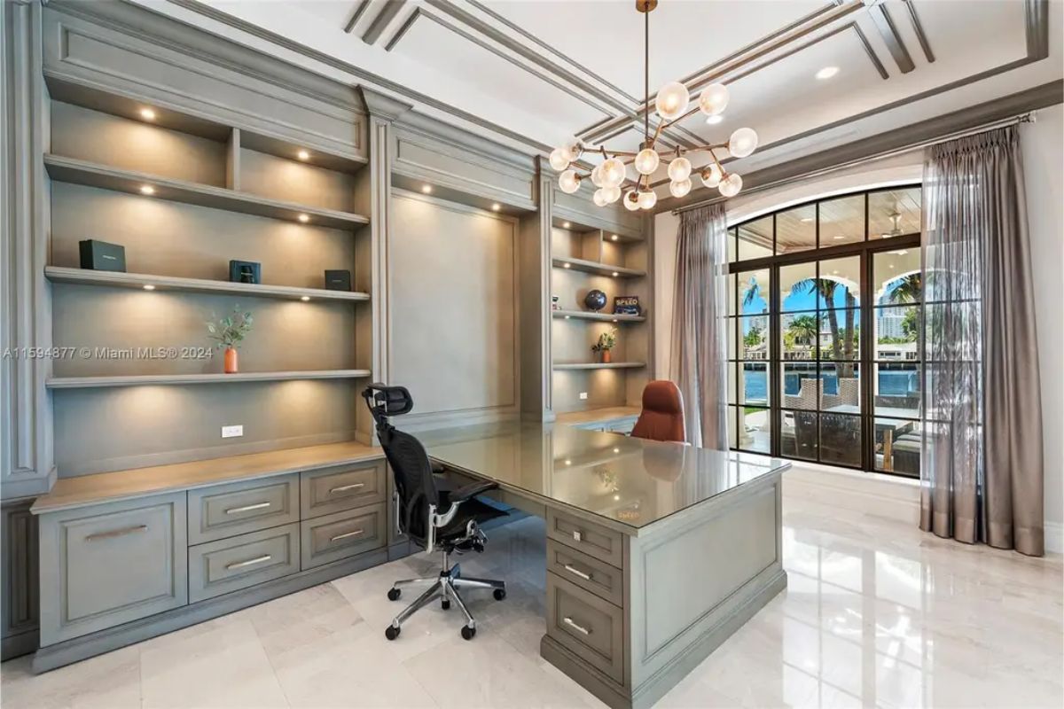 Home office includes built-in shelving, a glass-topped desk, and floor-to-ceiling windows facing the waterfront. 