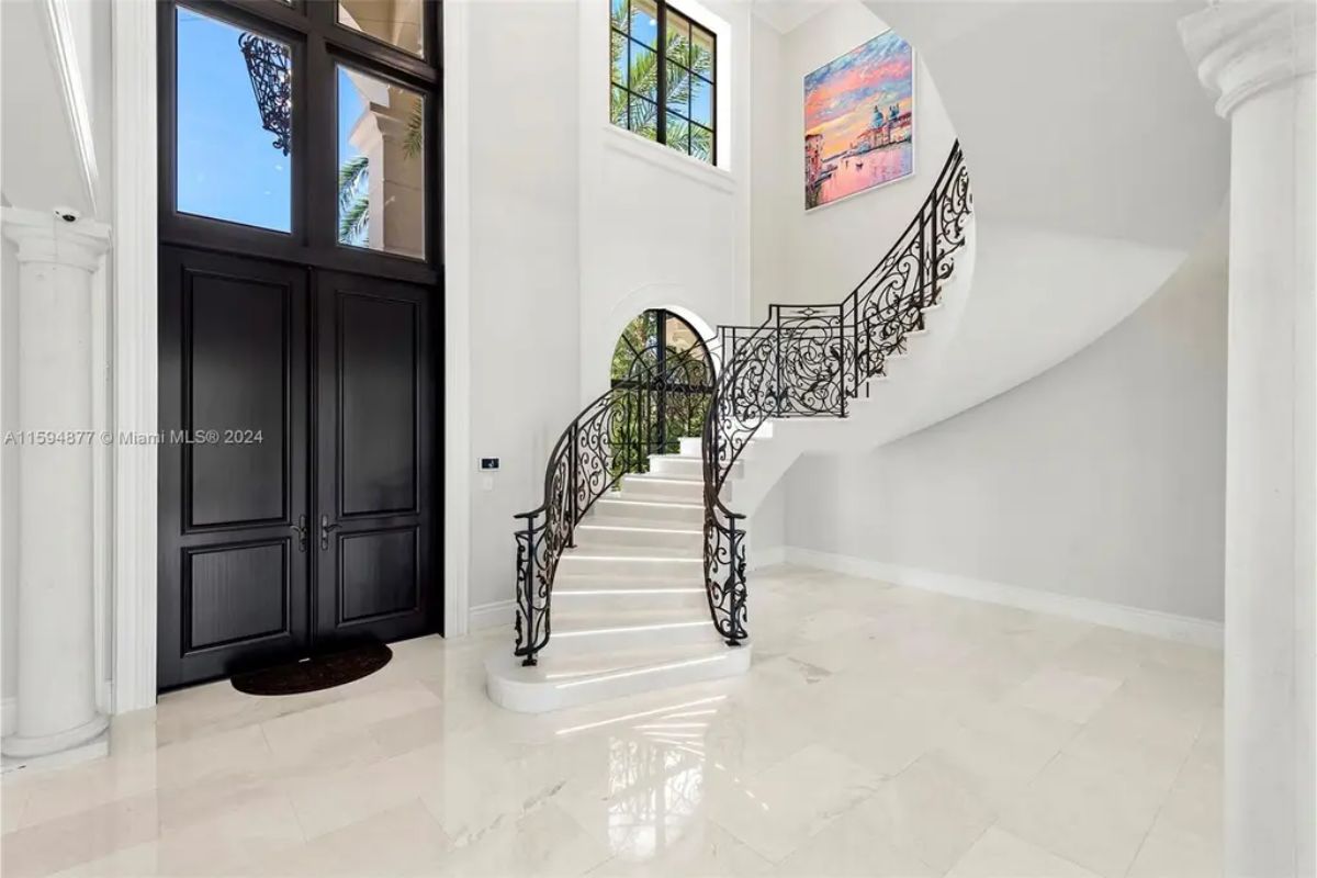 Grand interior entryway featuring a sweeping staircase with intricate wrought-iron railings and high ceilings. 