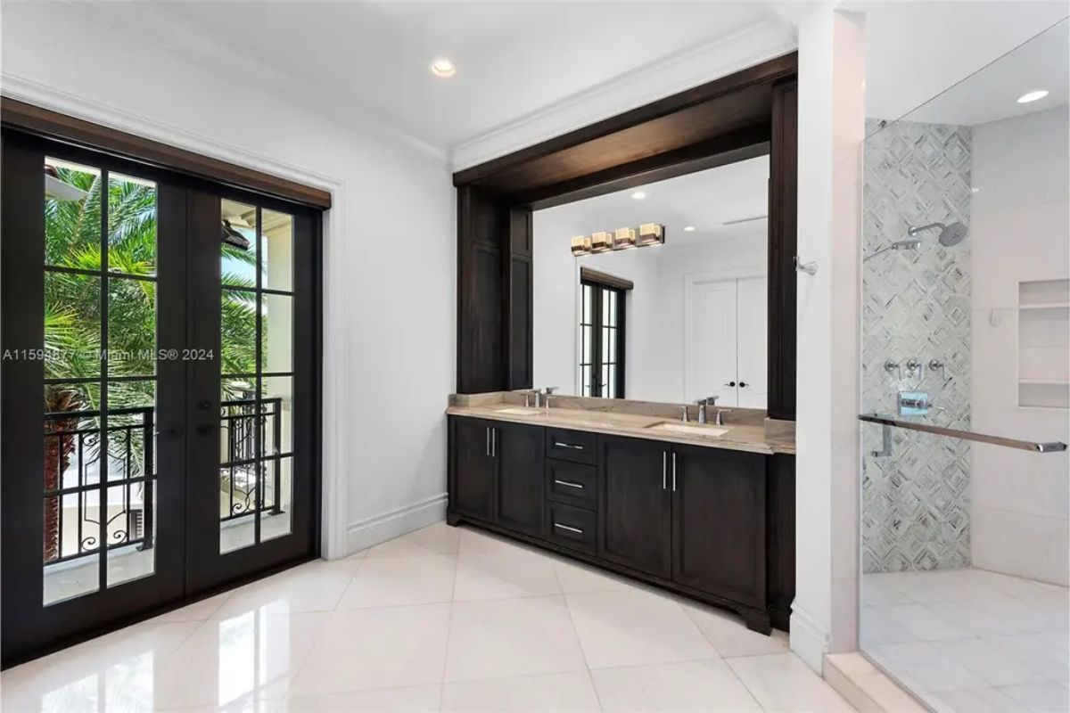 Elegant bathroom features a dual vanity with dark wood cabinets, a walk-in shower, and balcony access. 