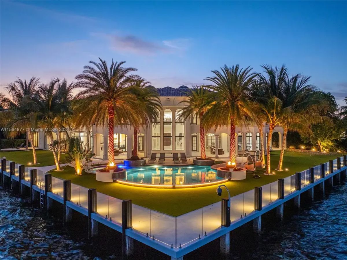 Close-up of the waterfront mansion showcasing a curved pool, palm trees, and vibrant lighting. 