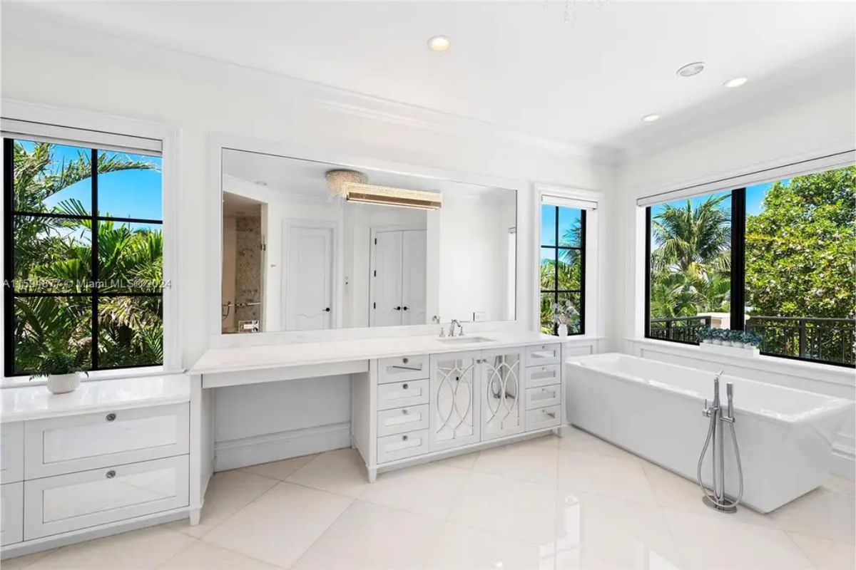 Bright bathroom with large vanity, standalone bathtub, and windows overlooking tropical greenery. 