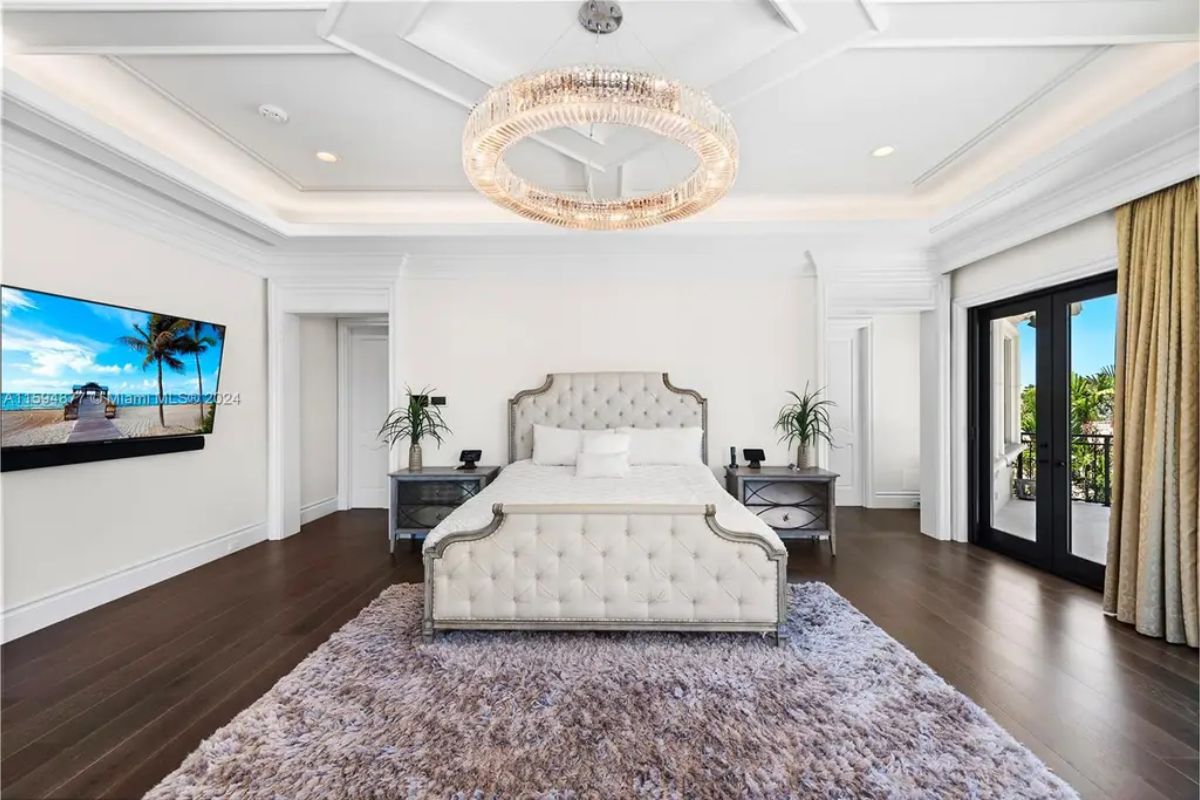 Spacious master bedroom features a luxurious bed, chandelier, and large windows with water views. 