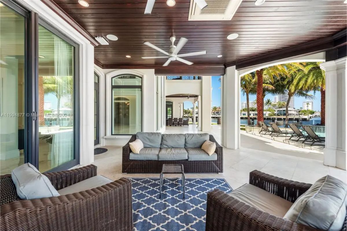 Outdoor patio area with wicker furniture under a covered veranda beside the pool. 