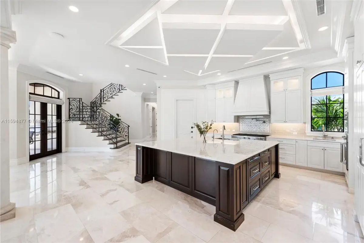 Open kitchen with a large marble island, custom cabinetry, and a staircase with ornate railings. 