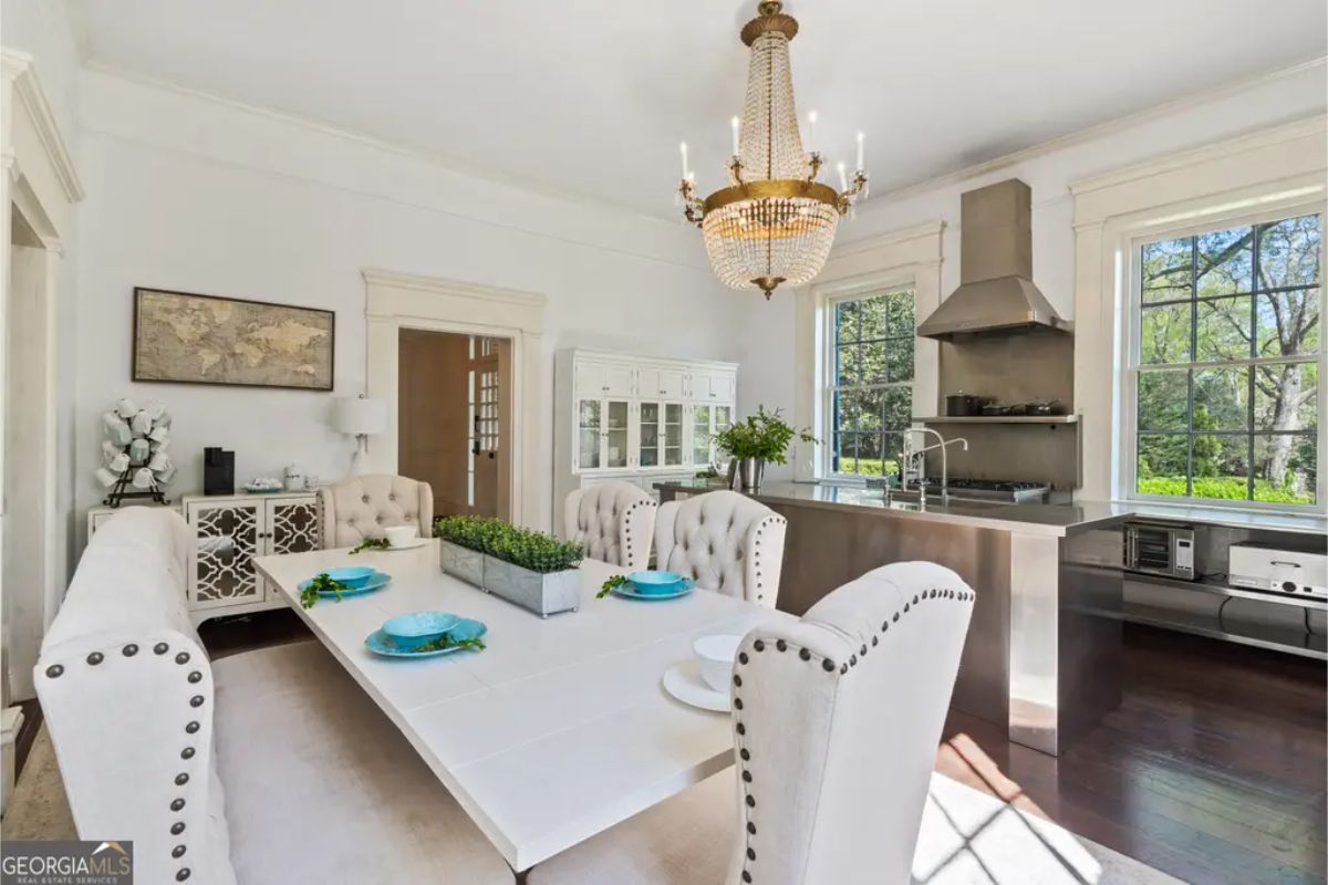 A large white dining table surrounded by tufted high-back chairs and a cushioned bench with nailhead trim.