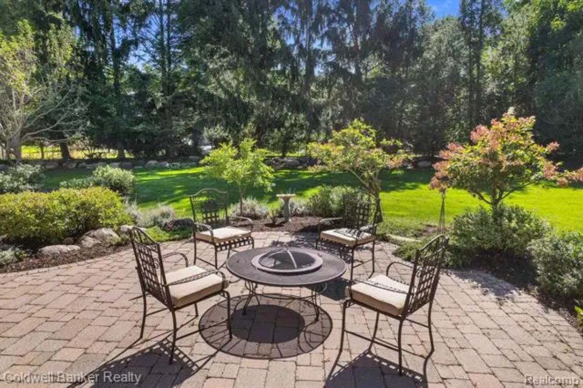 A paved patio surrounded by lush landscaping and mature trees.