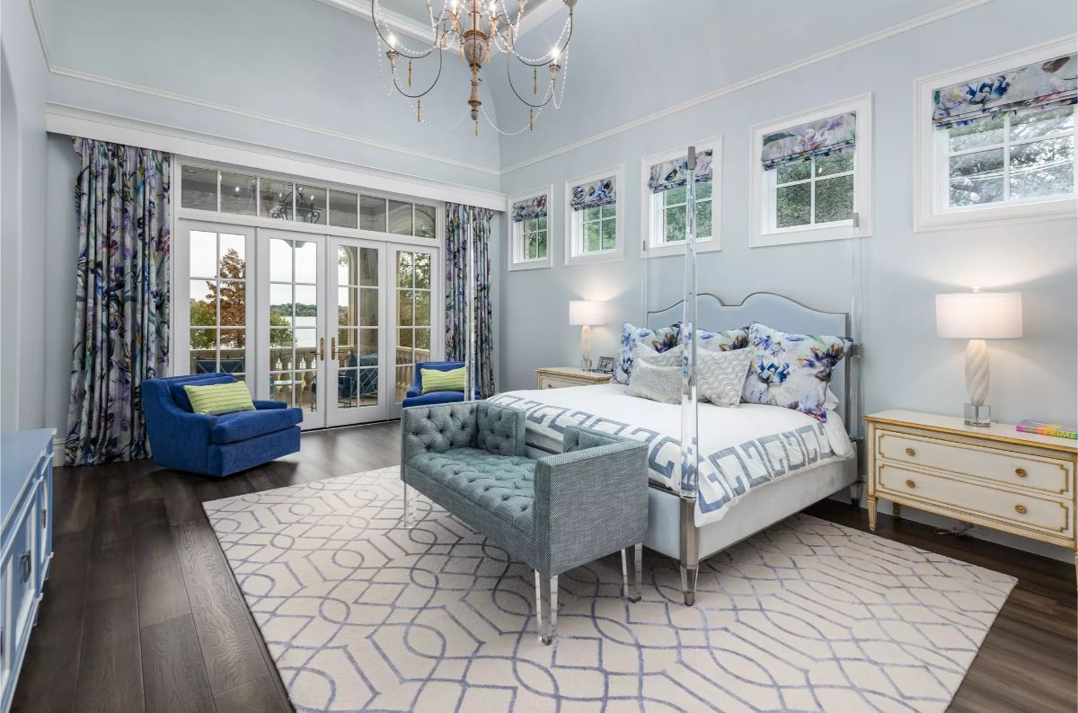 Luxurious bedroom featuring a high ceiling, soft blue tones, floral decor, and a balcony with a lake view. 