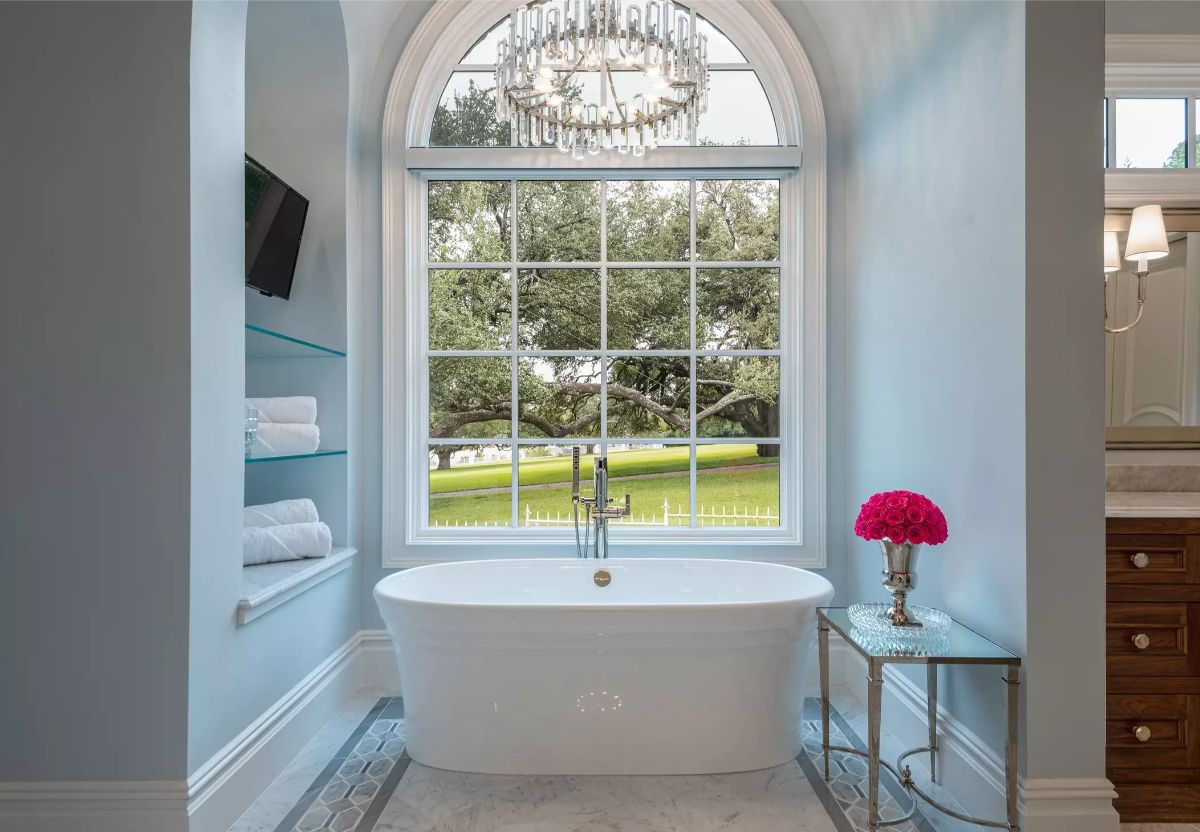 Spa-like bathroom showcasing a freestanding bathtub framed by a large arched window and a sparkling chandelier. 