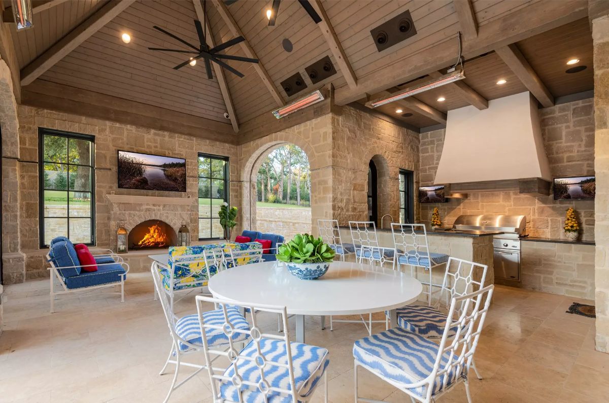 Outdoor pavilion featuring a stone fireplace, kitchen, and seating areas under a vaulted ceiling. 