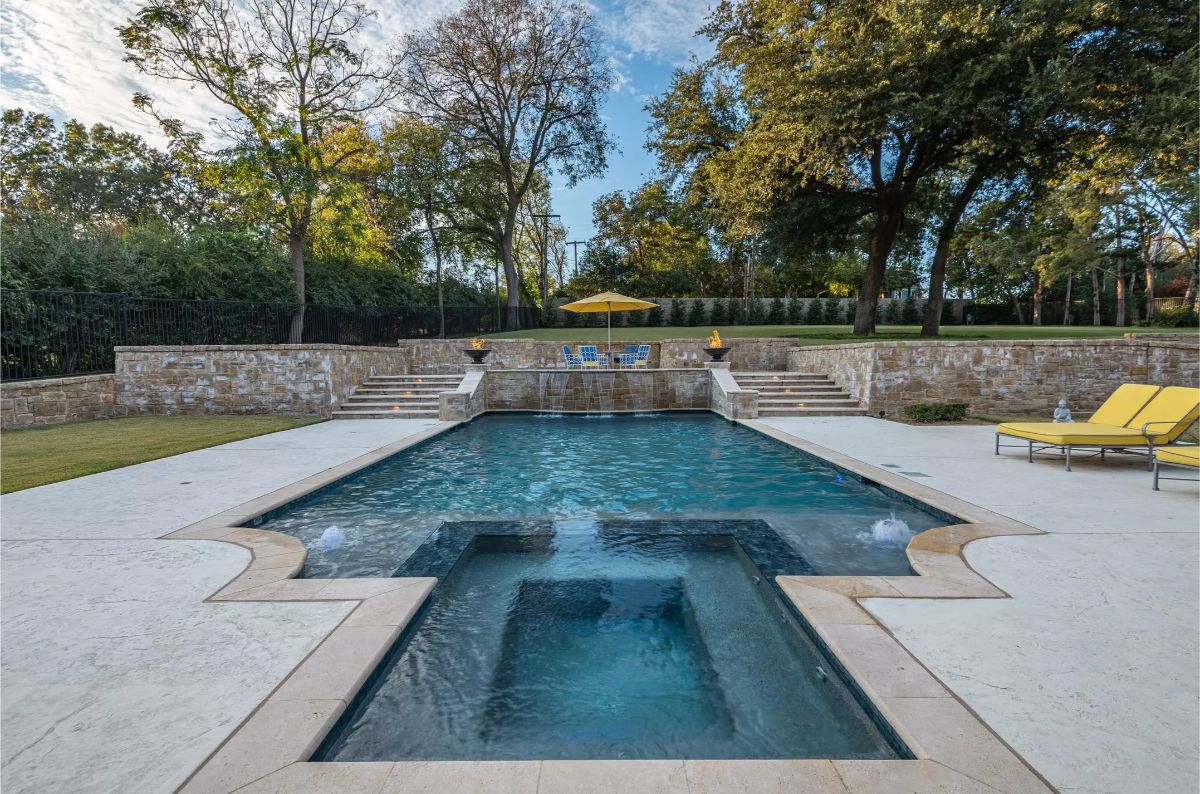 Swimming pool with a hot tub and cascading water features, framed by a landscaped garden. 