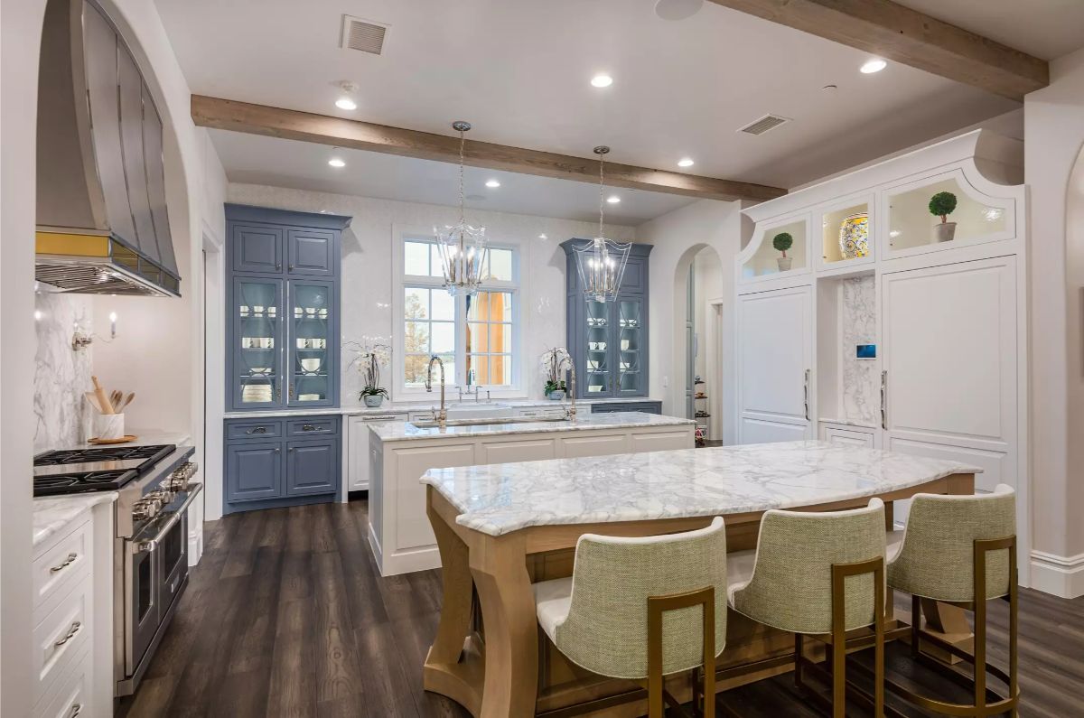 Kitchen with marble countertops, wooden and white cabinetry, and modern chandeliers under a beamed ceiling.