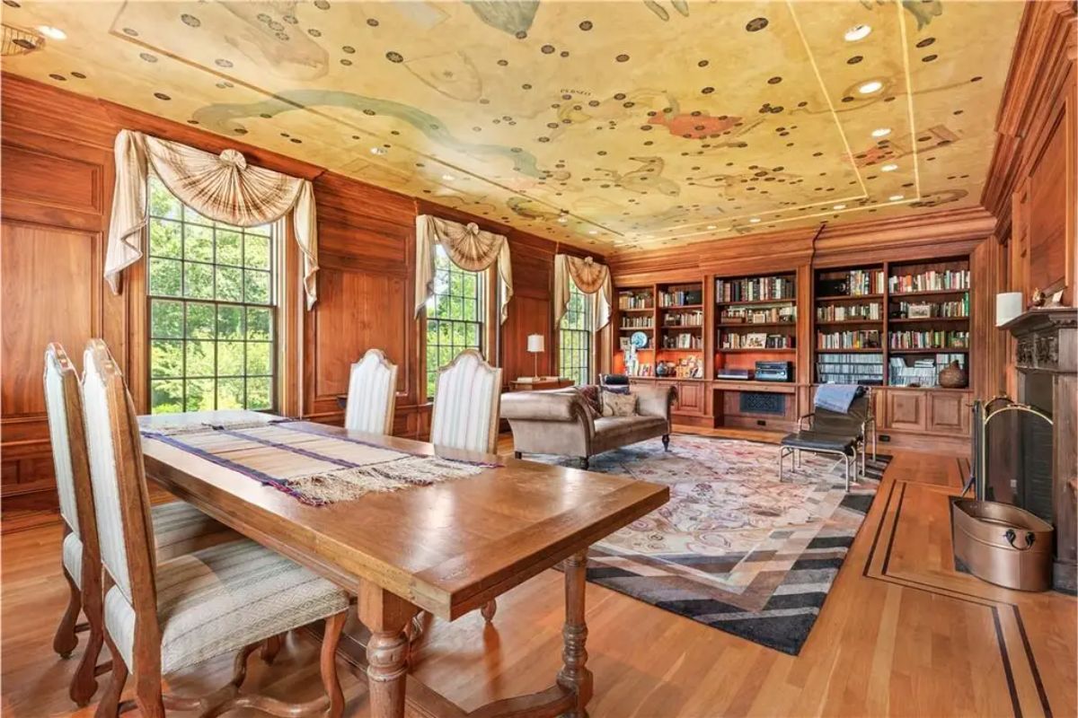 Elegant library with wood-paneled walls, a painted ceiling, and built-in bookshelves. 