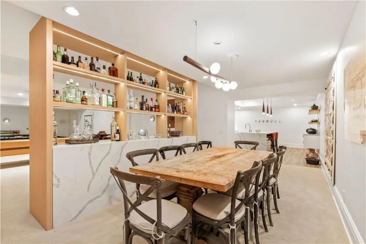 Well-lit bar and dining area with a wooden table, built-in shelving for beverages, and a marble counter. 