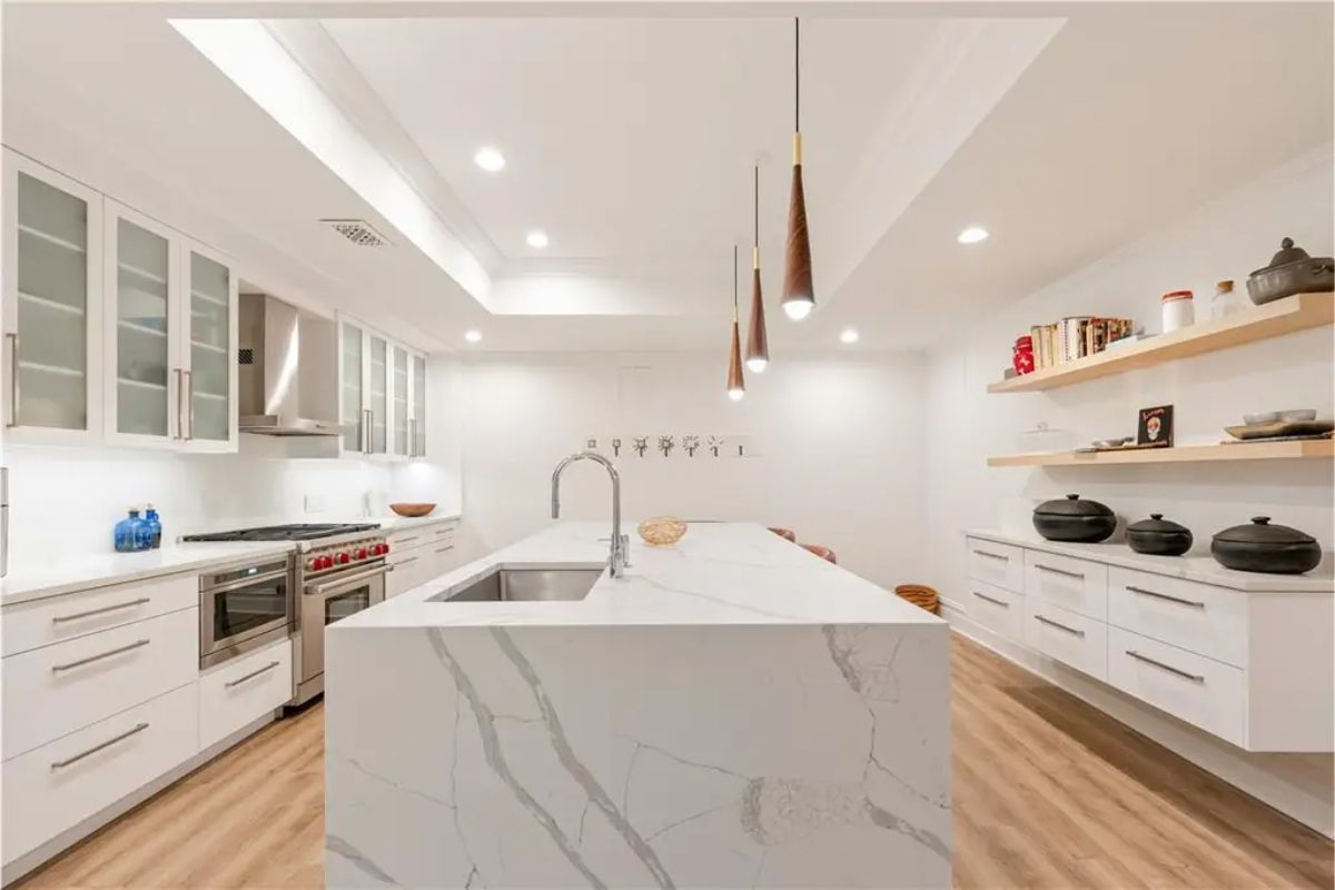 Bright kitchen featuring a marble island, pendant lights, and open shelving for storage. 