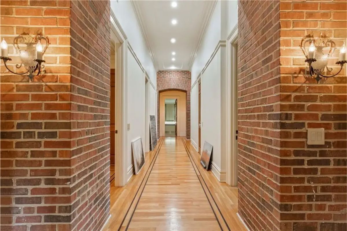 Hallway with exposed brick walls, wooden floors, and decorative wall sconces. 